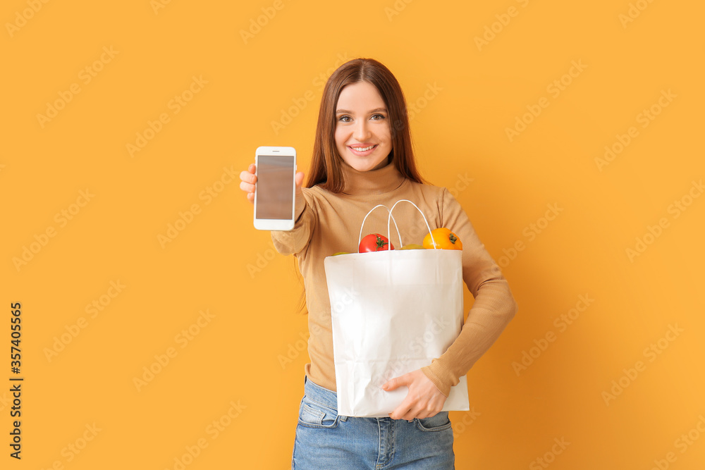 Young woman with food in bag and mobile phone on color background