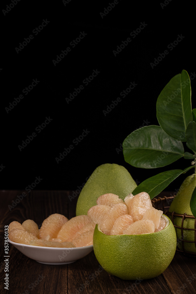 Fresh pomelo, pummelo, grapefruit, shaddock on wooden table over black background, close up, copy sp