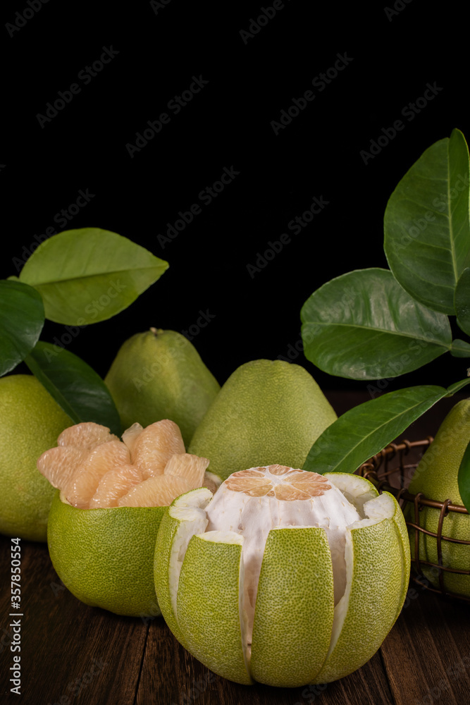 Fresh pomelo, pummelo, grapefruit, shaddock on wooden table over black background, close up, copy sp