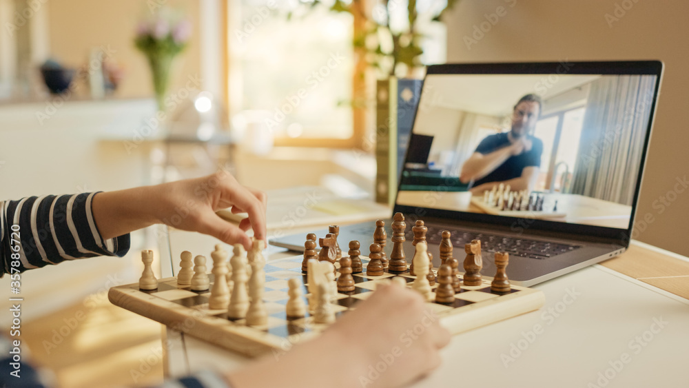 小男孩和他的国际象棋大师下棋，用笔记本电脑进行视频通话。孩子学习如何下棋