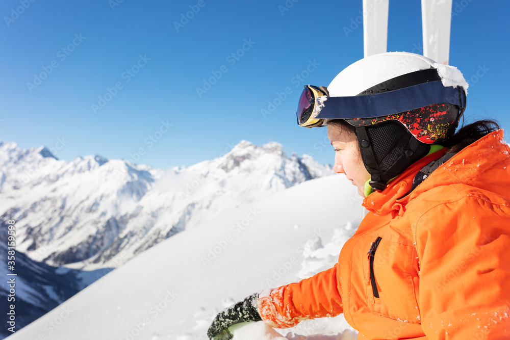 一个十几岁的女孩穿着橙色明亮的运动服，在高山上滑雪的近景