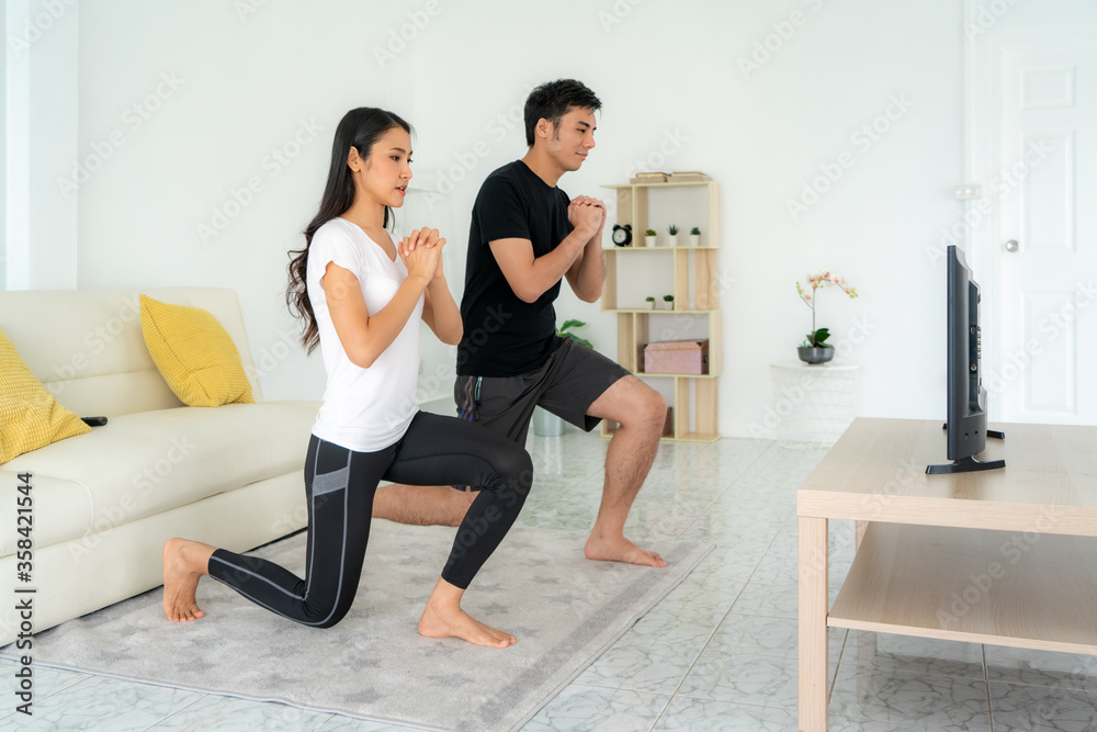 年轻的亚洲夫妇一起做深蹲训练，在家看电视，男人和女人一起锻炼