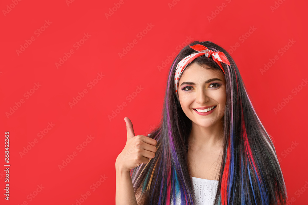 Beautiful young woman with unusual hair showing thumb-up on color background