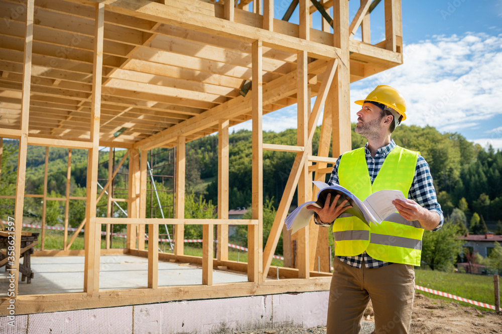 带蓝图的建筑工程师或建筑师参观木框架房屋建筑工地
