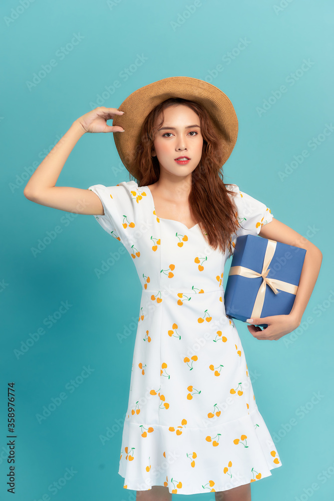 蓝色背景下，一位身穿连衣裙、戴着夏帽、拿着礼物盒的幸福女性的肖像