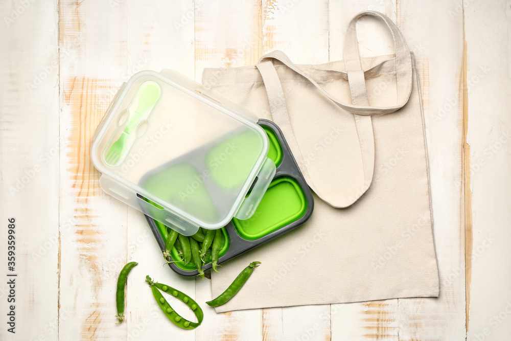 白色木质背景的带饭盒和绿豌豆的环保袋