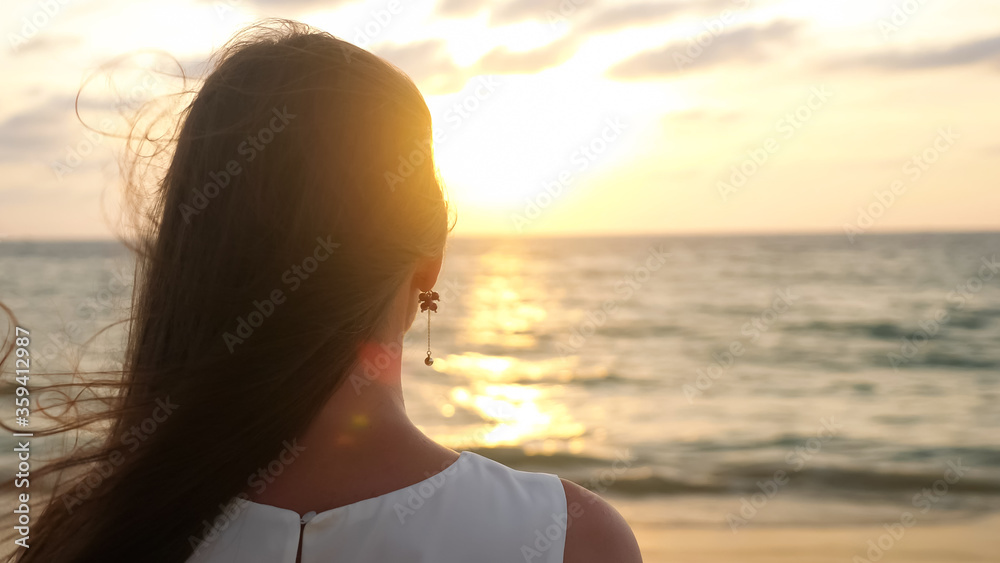 日落时分，一位留着蓬松长发的年轻女子站在热带度假胜地的沙滩上。