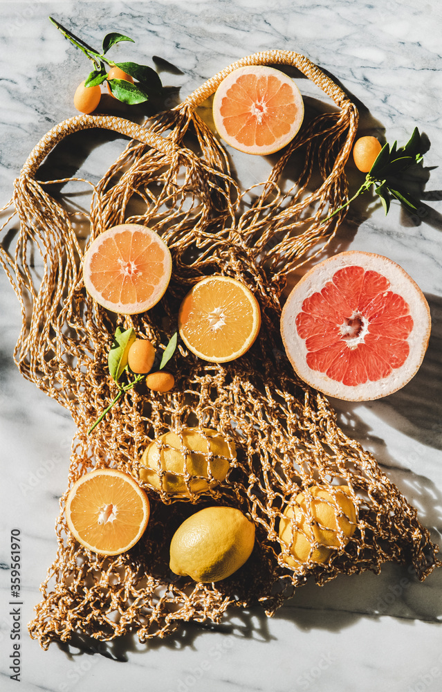 在灰色大理石背景下，放置各种新鲜成熟的柑橘类水果的夏季天然纸袋