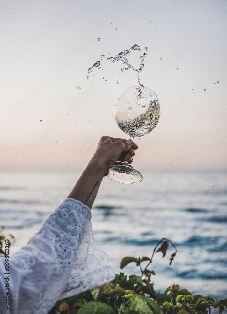 女人在美丽的日落色彩和背景下的地平线上，从酒窖中流出白葡萄酒。