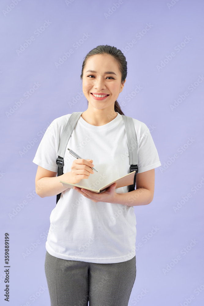 一个快乐的休闲女学生的画像，背着背包，拿着书站在记事本上写字