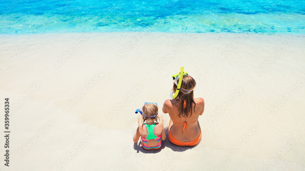 幸福的家庭-母亲，戴着浮潜面罩的女婴坐在热带岛屿的白色沙滩上。看