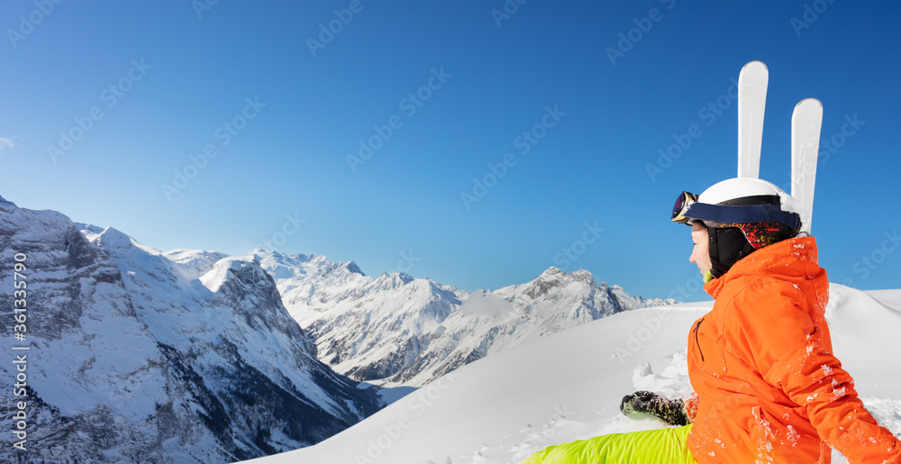 一个穿着橙色明亮运动服的可爱少女在高山上滑雪的背面肖像