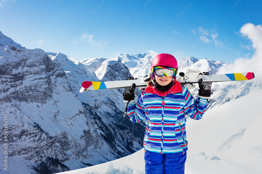 年轻微笑女孩的近照，她穿着五颜六色的衣服，戴着粉色头盔和彩色眼镜，在h上滑雪