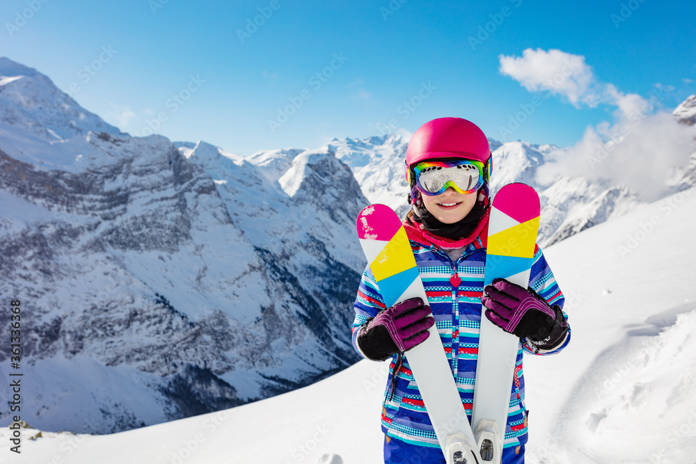 快乐可爱的女孩抱着一副滑雪鞋，戴着彩色眼镜和头盔，在巴茨的山峰上微笑