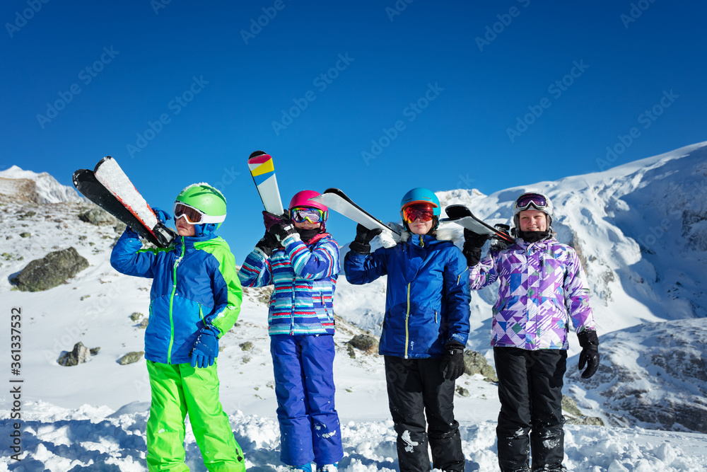 四个孩子一组，男孩和女孩肩上扛着滑雪板站在雪地里的山区度假胜地