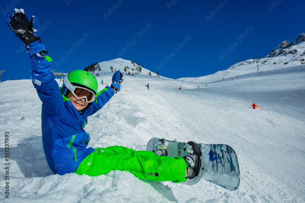 Close image of a little boy with snowboard sit on the snow view from side in mask, ski helmet liftin