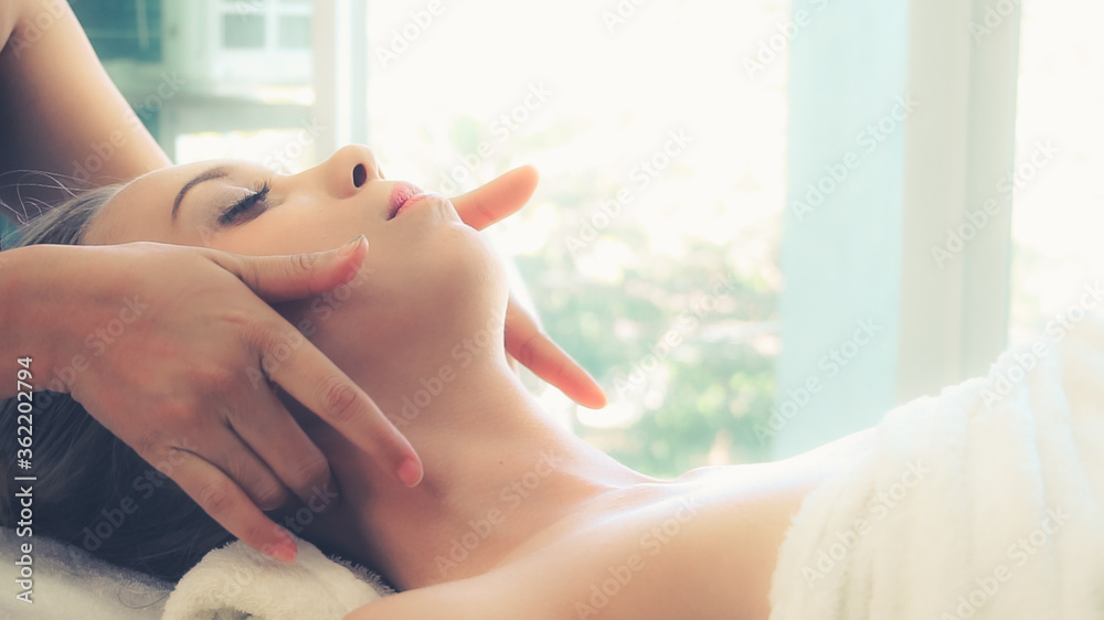 放松的女人躺在水疗床上，接受按摩治疗师的面部和头部按摩水疗