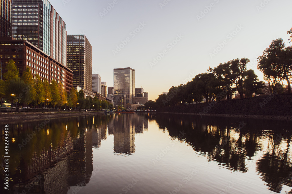 Warm Tokyo skyline and trees with reflections in still water after sunset seen from Imperial Palace 