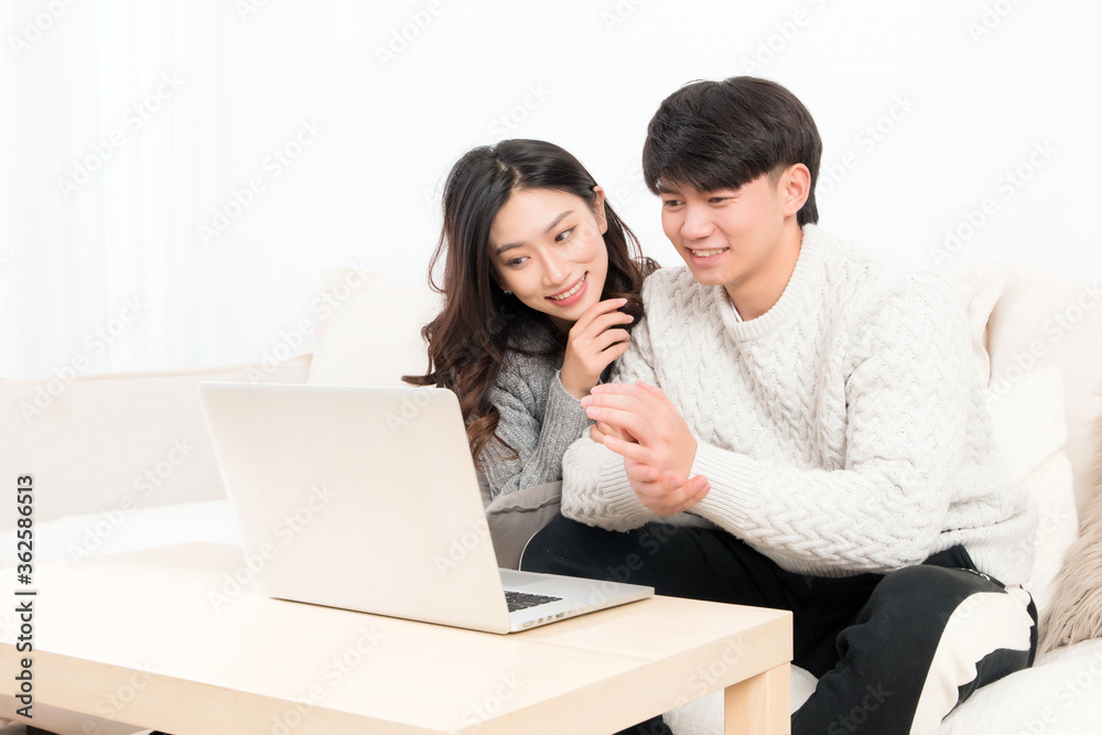 冬天，一对亲密的亚洲年轻情侣坐在沙发上，开心地玩电脑