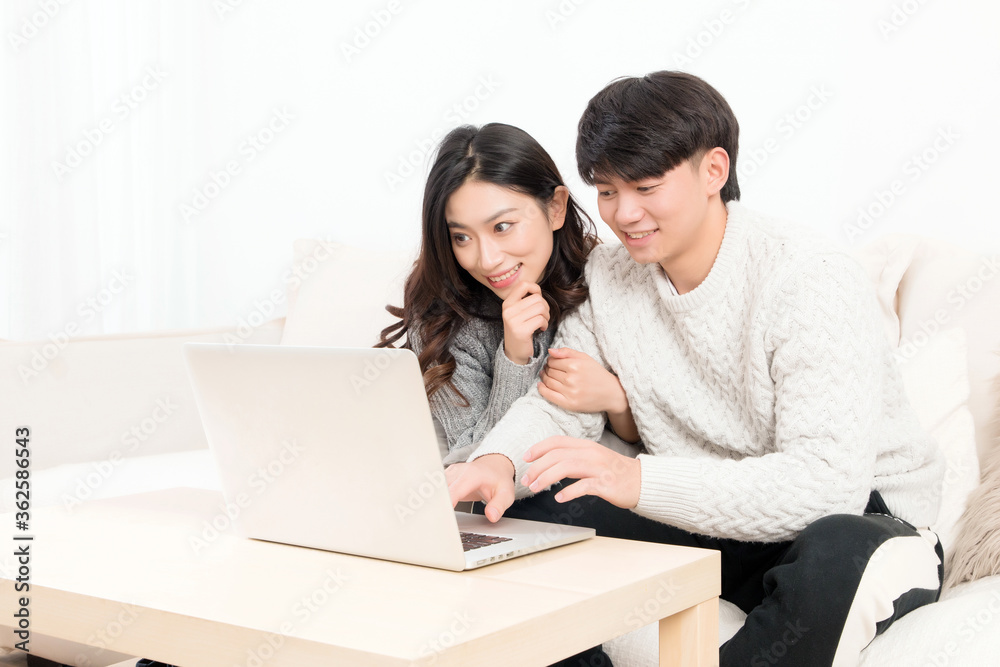 冬天，一对亲密的亚洲年轻情侣坐在沙发上，开心地玩着电脑
