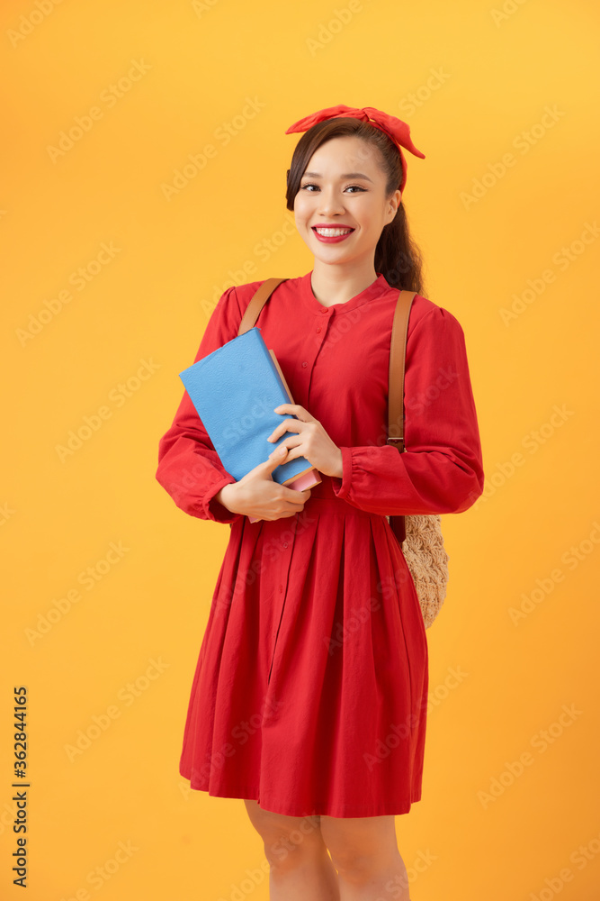漂亮的亚洲学生拿着书，带着橙色背景的袋子。