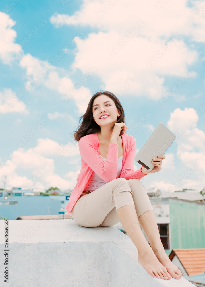 Elegant young Asian woman reading book while sitting on rooftop.