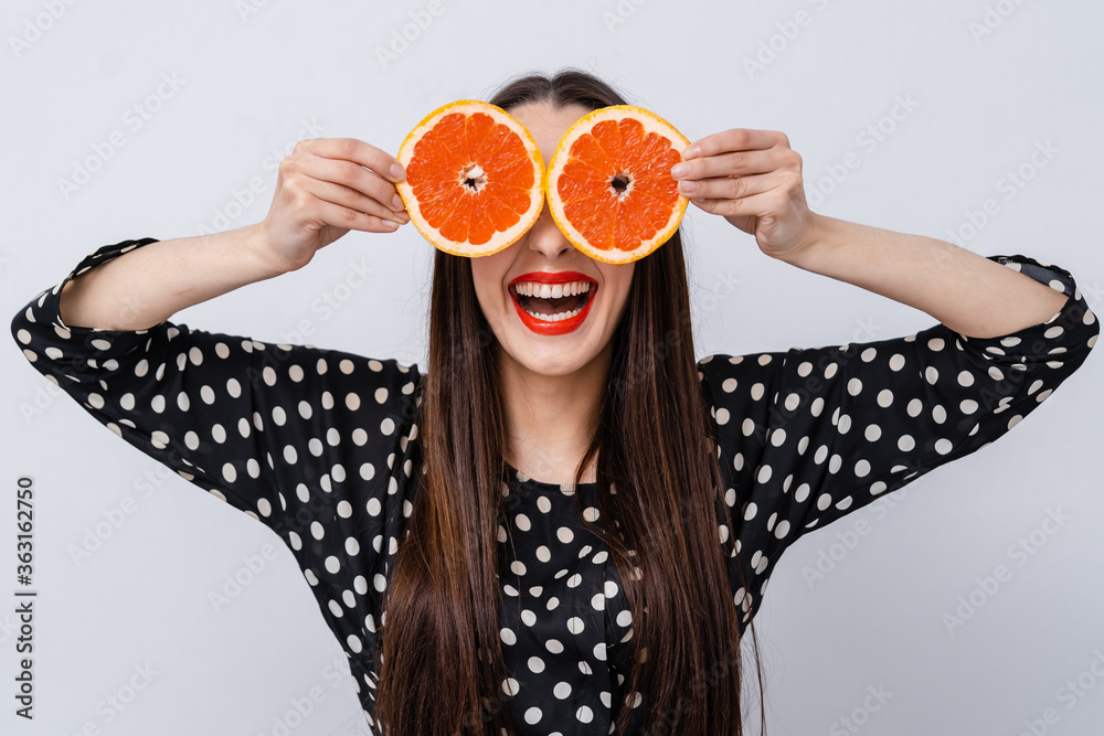 快乐的女孩把葡萄柚的两半举到眼睛附近。疯狂素食主义者的概念。面部表情
