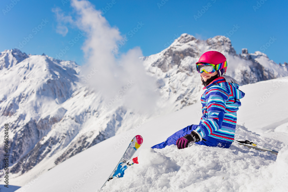 快乐的年轻女孩，穿着鲜艳的运动服，坐在高山上的雪堆上，看起来很巴