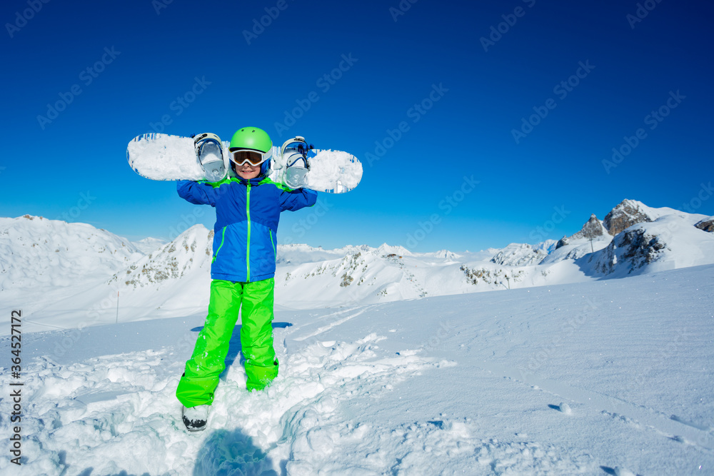 一个男孩肩上扛着滑雪板站在山顶雪地里的快乐全高肖像