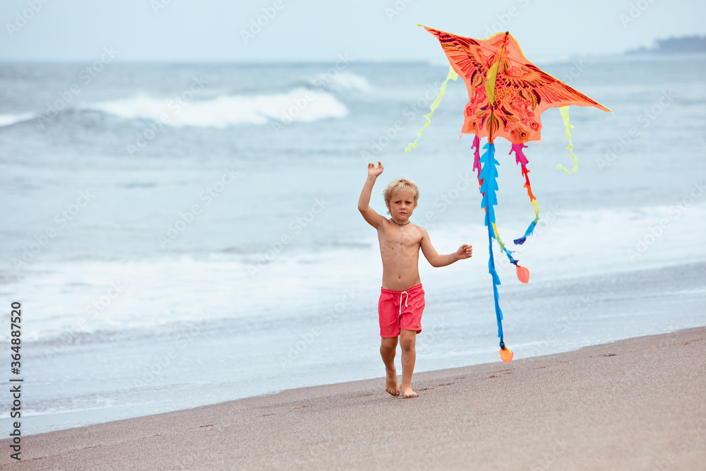 快乐的一家人在热带海滩度假胜地玩得很开心。有趣的小男孩带着风筝沿着海浪奔跑