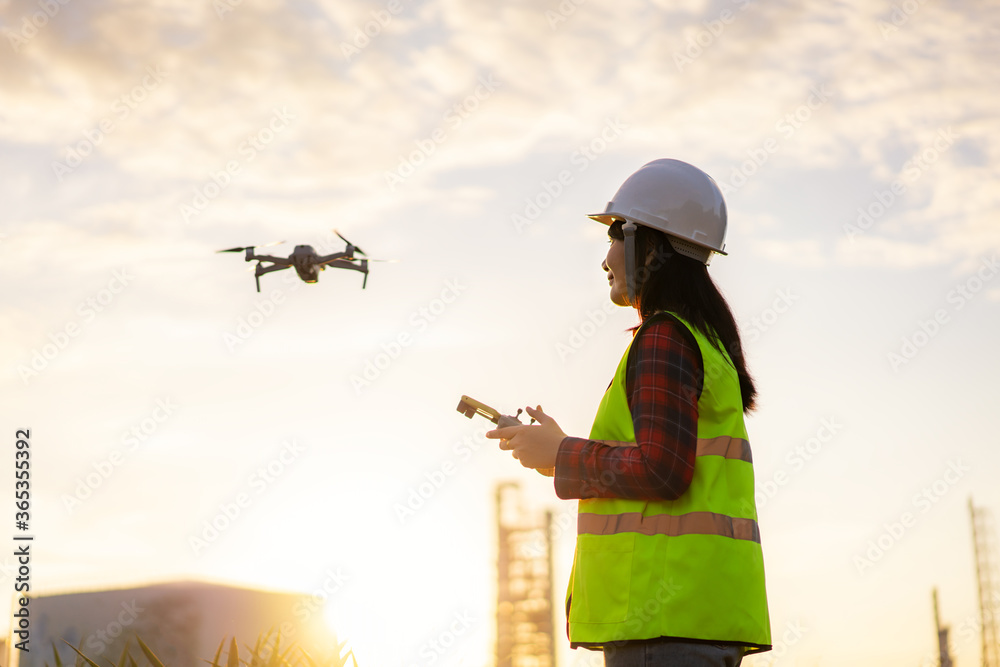 亚洲女工程师在日出建筑工地勘察期间在炼油厂上空操作无人机