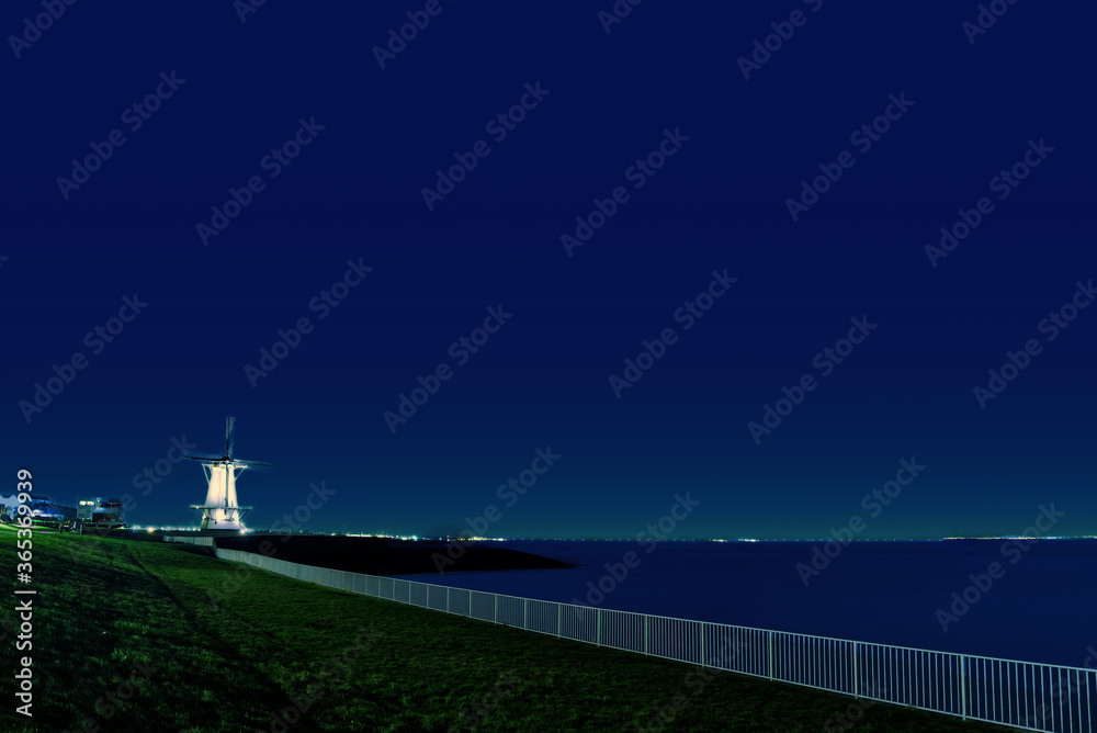 深蓝色天空下的海边栏杆和风车，宁静的夜晚，荷兰的瓦利辛根