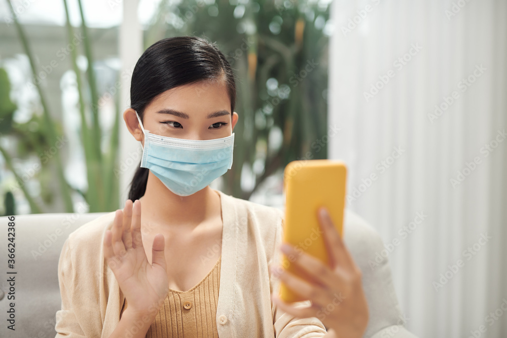 戴着口罩在家用智能手机视频通话的休闲病女性，