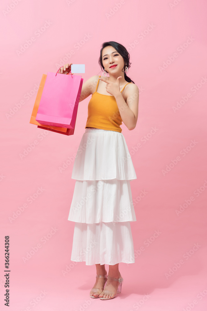 站在粉色背景下，拿着五颜六色的购物袋，全身兴奋的亚洲女人。