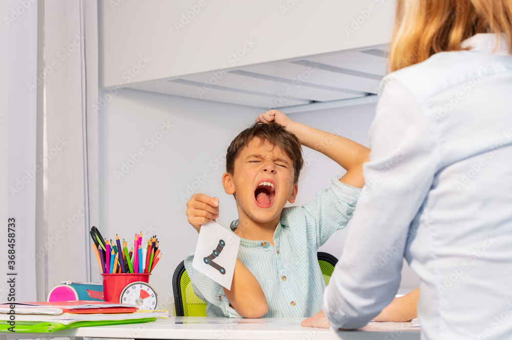 Boy with autism spectrum disorder tear hairs and scream expressing negative emotions while learning 