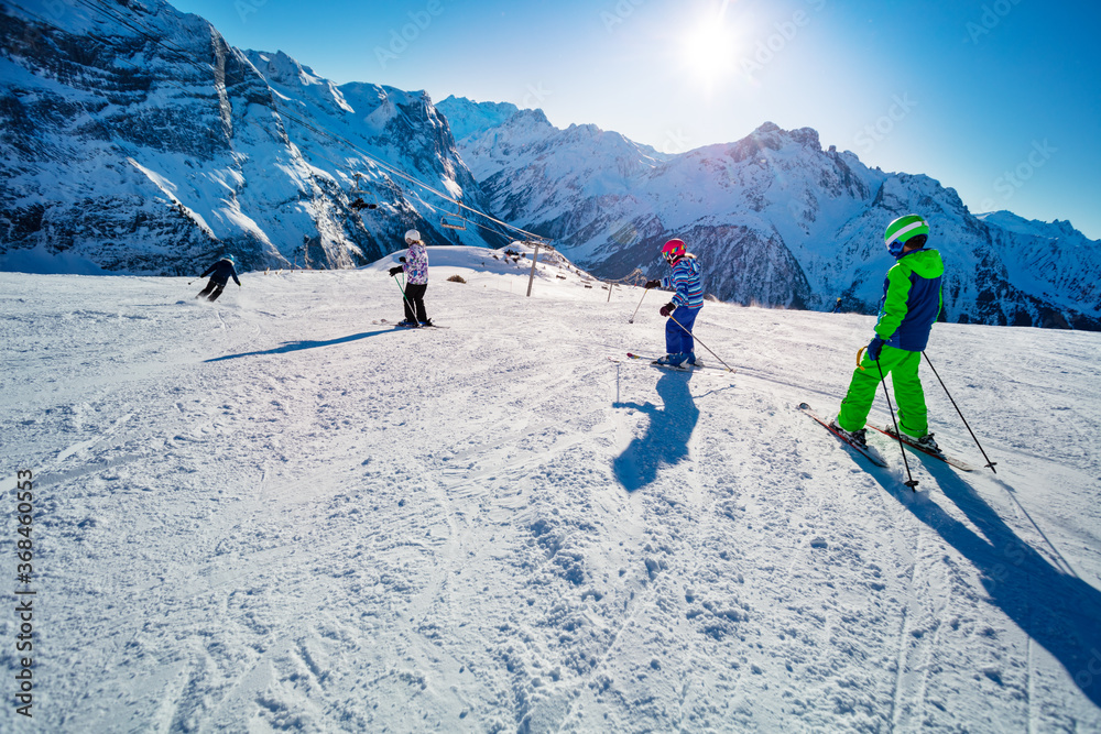 四个孩子在阿尔卑斯山斜坡上以学校队形一起滑雪，一个接一个地从贝希看风景
