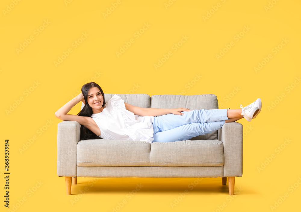 年轻女子在彩色背景下的沙发上放松