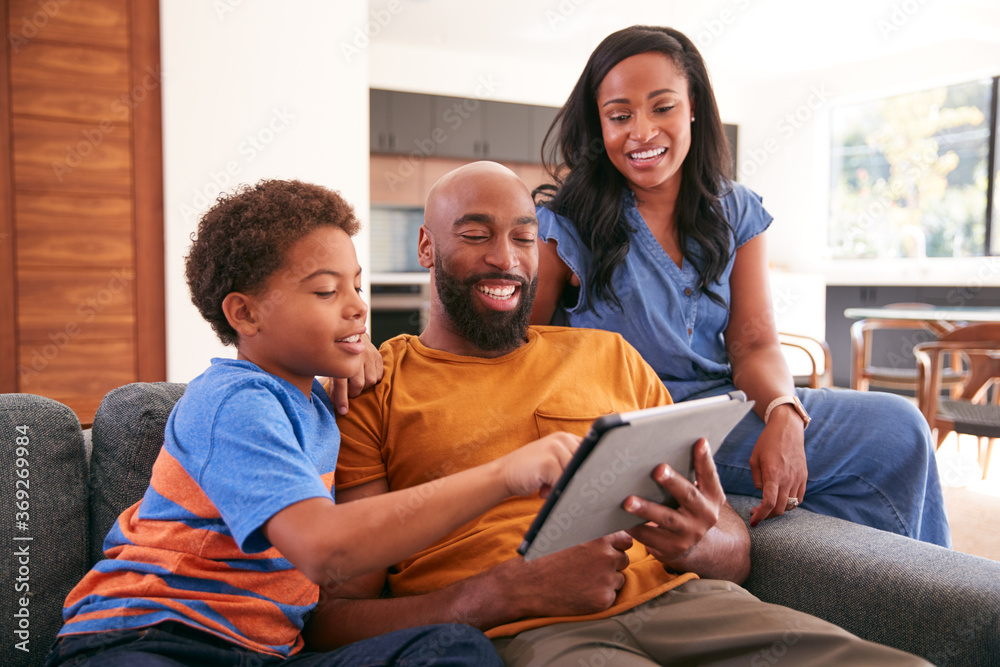 儿子坐在沙发上的非裔美国人家庭在家使用数字平板电脑