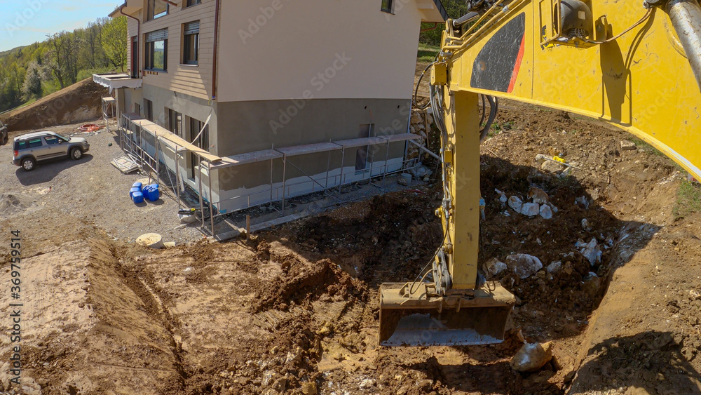 POV：使用卡特彼勒挖掘机在未完工的房屋附近挖掘土壤。