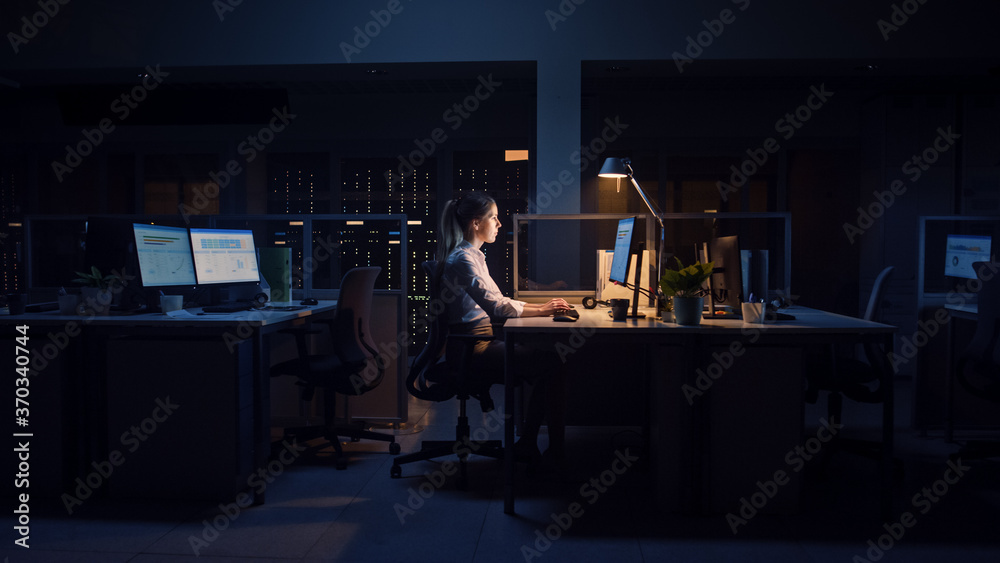 在办公室工作到深夜：女商人使用台式电脑，分析，使用文档