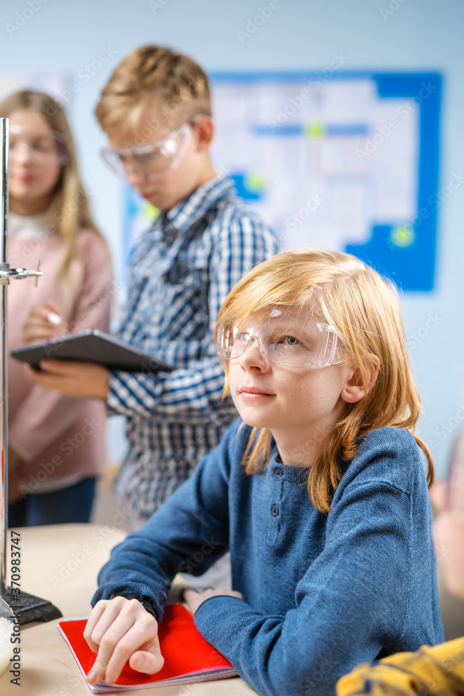 一个戴着安全眼镜的可爱小男孩的肖像，坐在化学科学的学校桌子旁