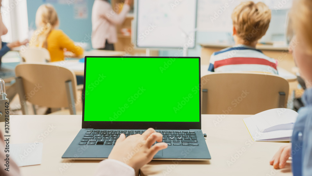 小学科学课：小女孩使用带有绿色屏幕模型模板的笔记本电脑。在B中
