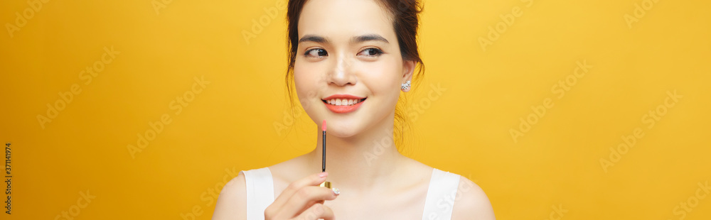 完美女孩拿着黄色背景上的口红，特写肖像。