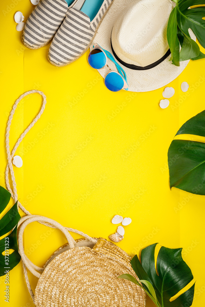 黄色背景下的草帽、相机、包、夏鞋、太阳镜、贝壳和热带树叶