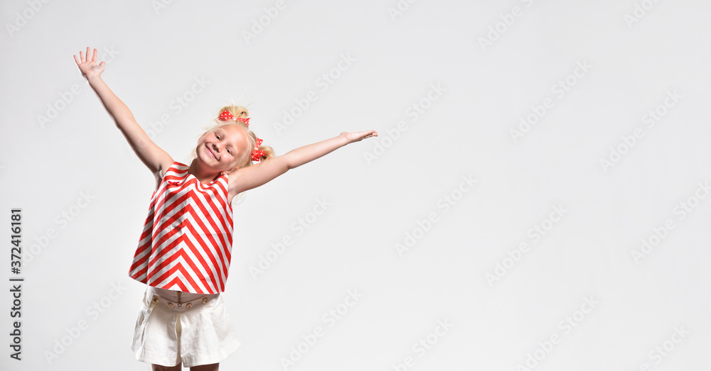Blonde girl 7 years old smiles and opened her arms wide on a gray background with copy space