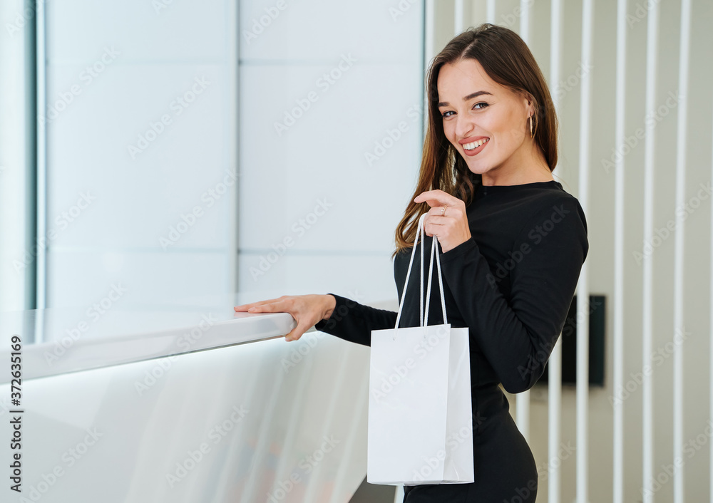 女人拿着白色背景的购物袋。白色纸袋。现代办公室背景。