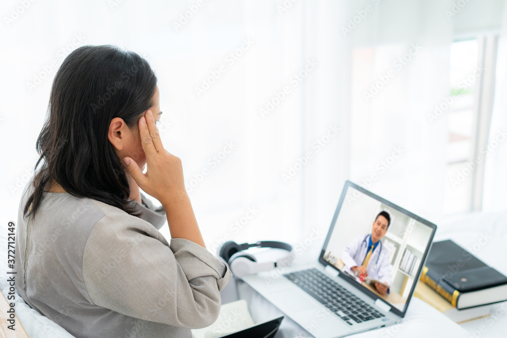 Asian woman in white bed speaking with doctor using tele health technology while sitting on a sofa a