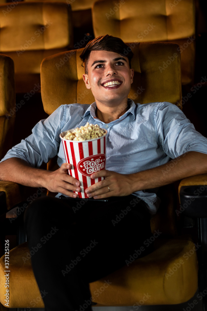 一个年轻人在电影院看电影时微笑着享用爆米花