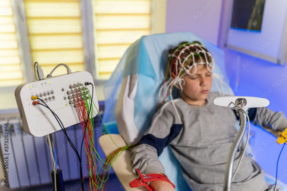 在脑电图检查中，戴着特殊医用帽的男孩，旁边是带读数的监视器。