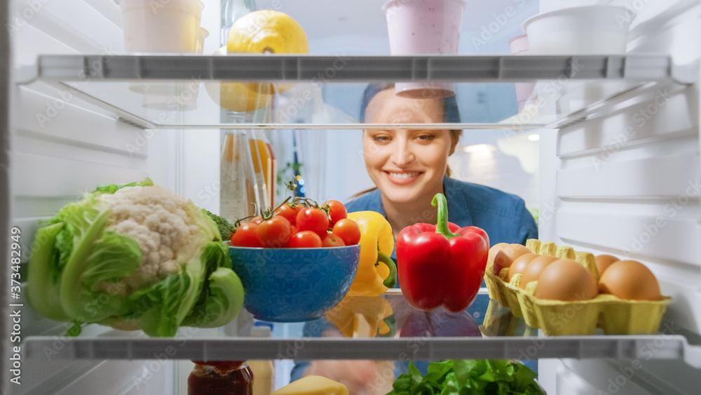漂亮年轻女人看冰箱里拿出蔬菜。女人在准备健康餐